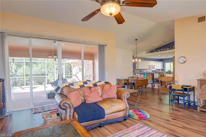 Living room with wood finished floors, vaulted ceiling, and ceiling fan with notable chandelier