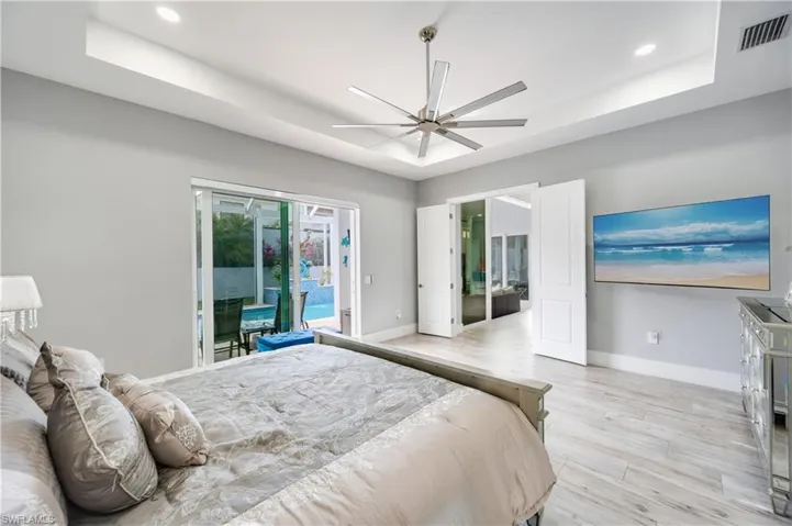 Bedroom with a tray ceiling, light wood-style flooring, ceiling fan, access to outside, and recessed lighting
