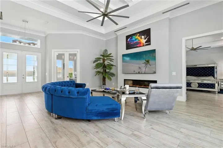 Living area with french doors, a ceiling fan, a high ceiling, crown molding, and a glass covered fireplace