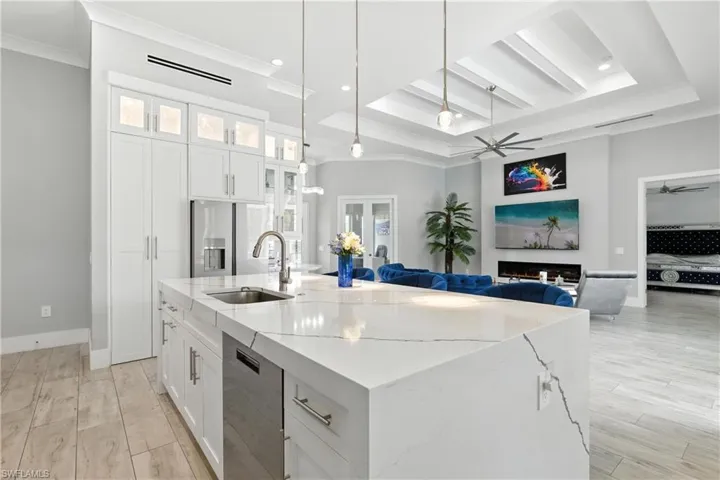 Kitchen with dishwasher, a ceiling fan, ornamental molding, a center island with sink, and light stone counters