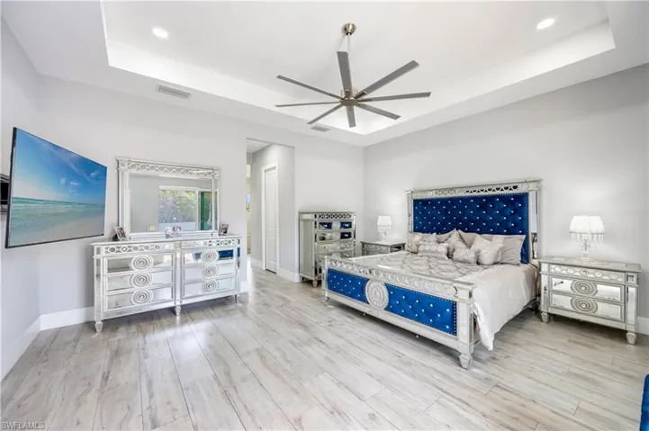 Bedroom with a tray ceiling, ceiling fan, light wood-style floors, and recessed lighting