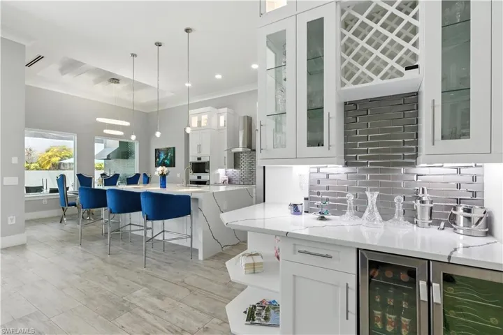 Bar area featuring backsplash, wall chimney range hood, pendant lighting, ornamental molding, and wine cooler