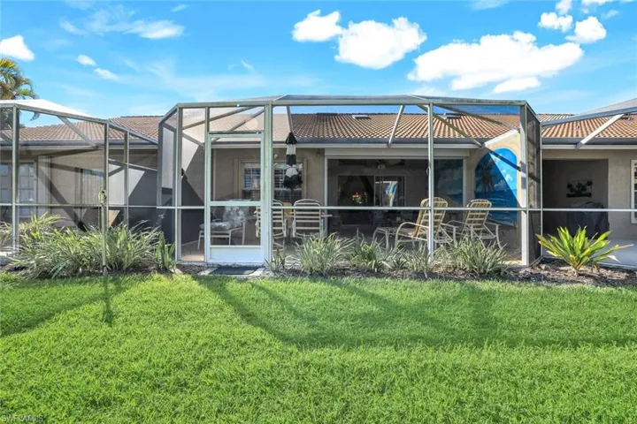 Back of property with a tile roof, glass enclosure, and a lawn