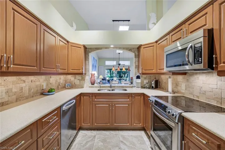 Kitchen with stainless steel appliances, light countertops, brown cabinets, and a sink