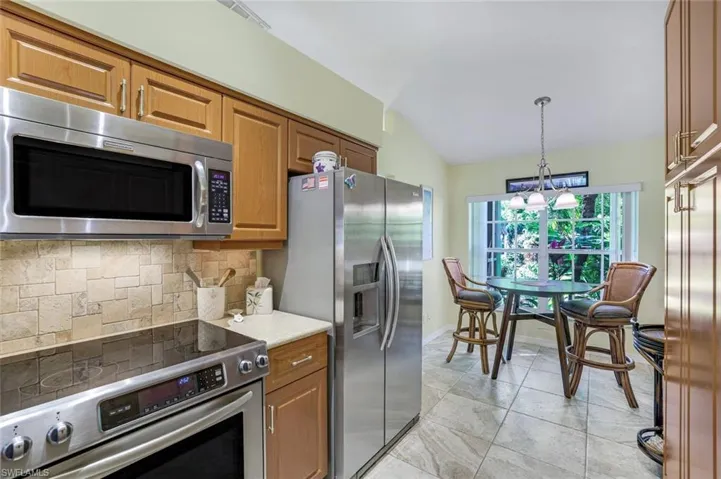 Kitchen featuring brown cabinets, tasteful backsplash, lofted ceiling, light countertops, and appliances with stainless steel finishes