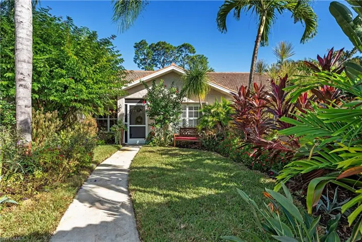 View of property hidden behind natural elements with a front yard, a tile roof, and stucco siding