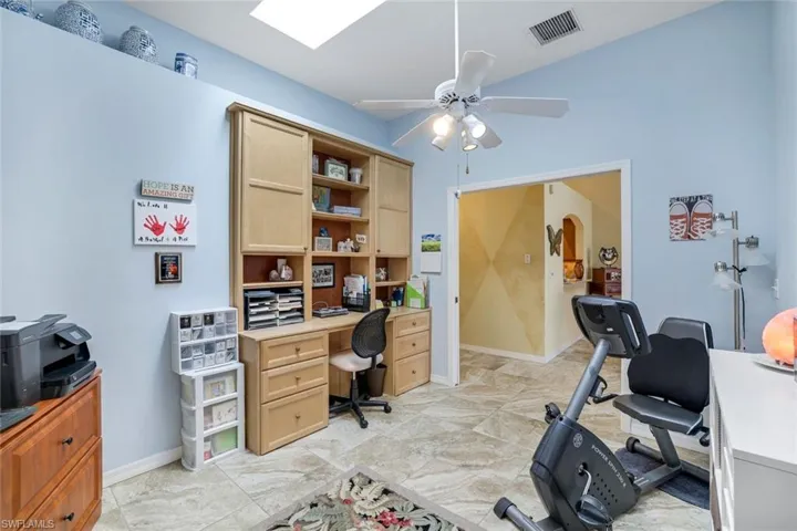 Office area featuring arched walkways, baseboards, visible vents, and a ceiling fan