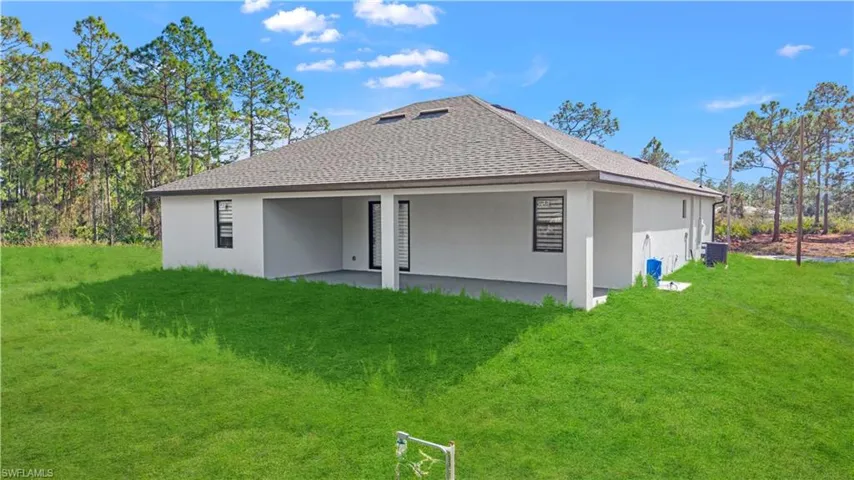 Rear view of house featuring a shingled roof, a lawn, and stucco siding