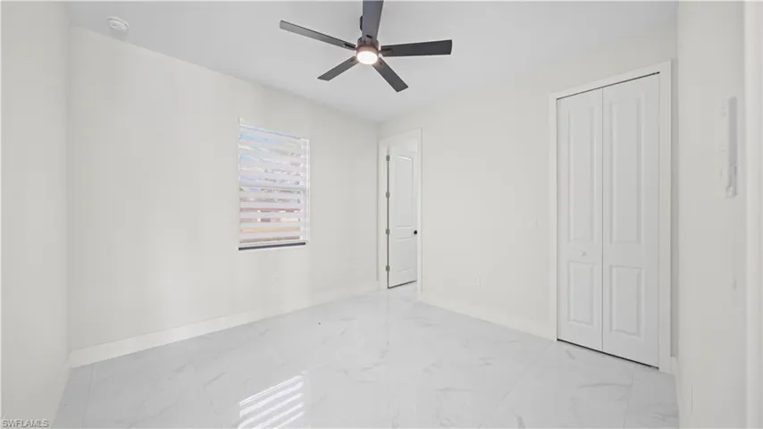 Unfurnished bedroom featuring light marble finish flooring, a ceiling fan, and a closet