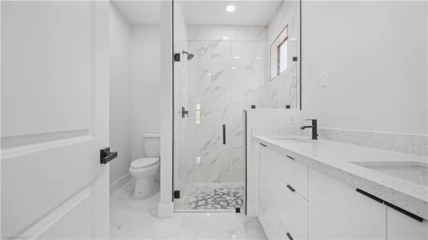 Full bath with double vanity, a marble finish shower, light marble finish floors, and recessed lighting
