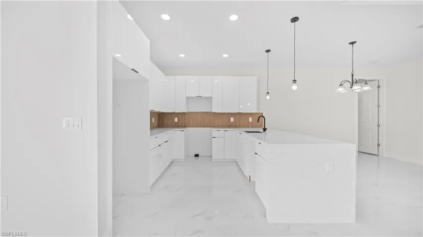 Kitchen with modern cabinets, white cabinetry, a peninsula, light stone countertops, and decorative light fixtures