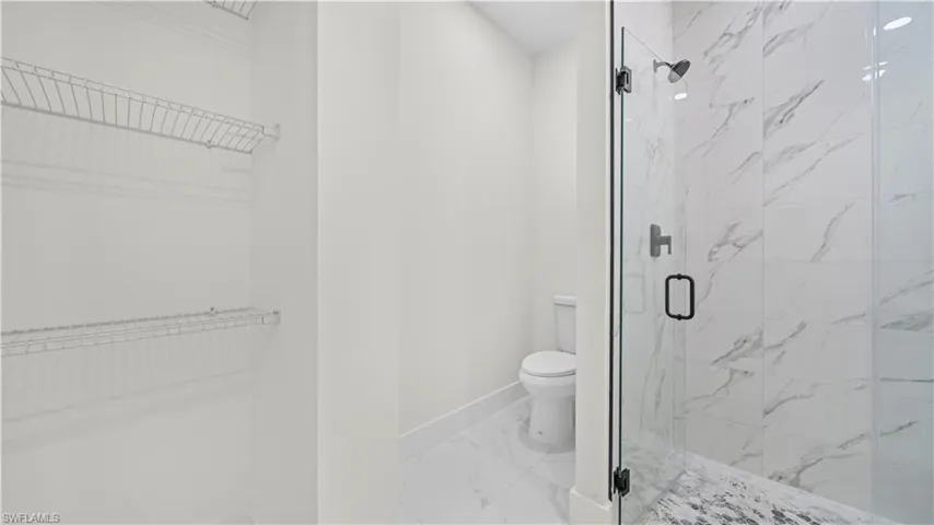Bathroom featuring a walk in closet, light marble finish floors, and a marble finish shower