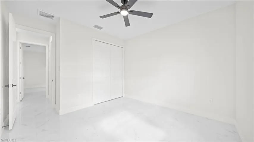 Unfurnished bedroom featuring light marble finish floors, ceiling fan, and a closet
