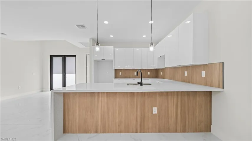 Kitchen with modern cabinets, white cabinets, a peninsula, light stone counters, and recessed lighting