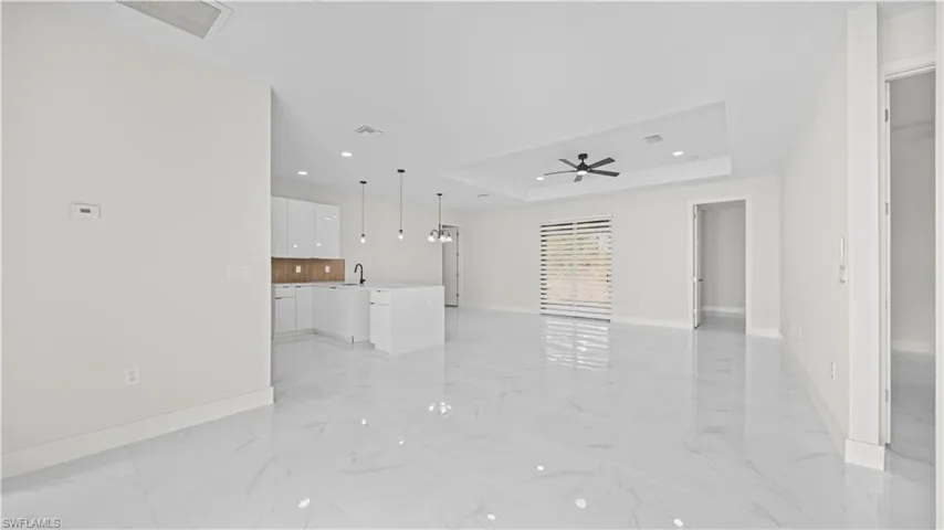Unfurnished living room with a raised ceiling, recessed lighting, light marble finish floors, and a chandelier