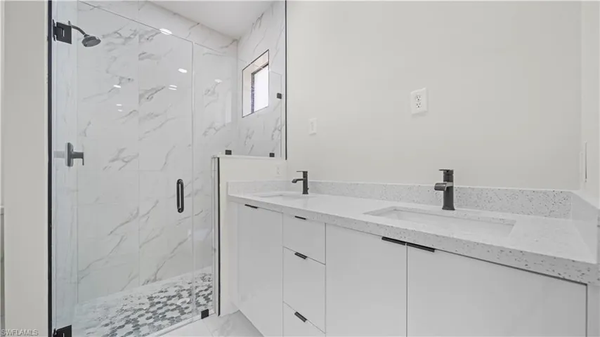 Full bathroom with double vanity and a marble finish shower
