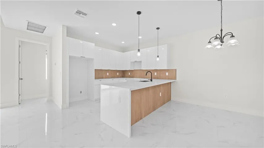 Kitchen with modern cabinets, white cabinets, hanging light fixtures, a peninsula, and light stone counters