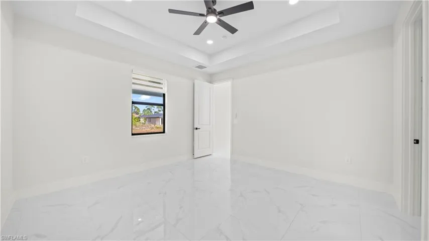 Empty room with a raised ceiling, light marble finish floors, a ceiling fan, and recessed lighting