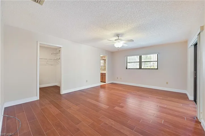 Unfurnished bedroom featuring a walk in closet, wood-type flooring, ceiling fan, and connected bathroom