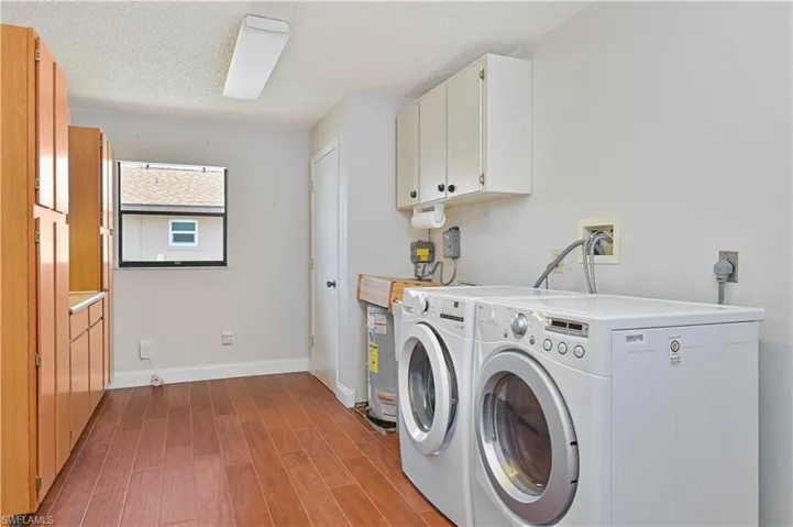 Laundry room with cabinet space, a textured ceiling, dark wood-style Tile flooring, laundry tub and washing machine and dryer