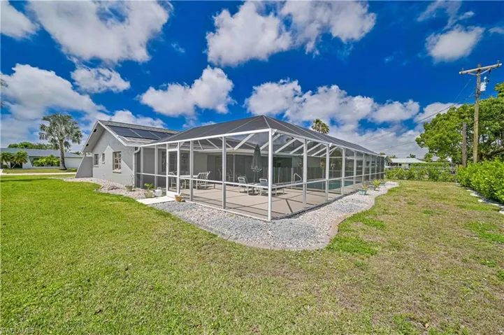 Rear view of house with screened enclosure, a sunroom, a lawn, and a pool