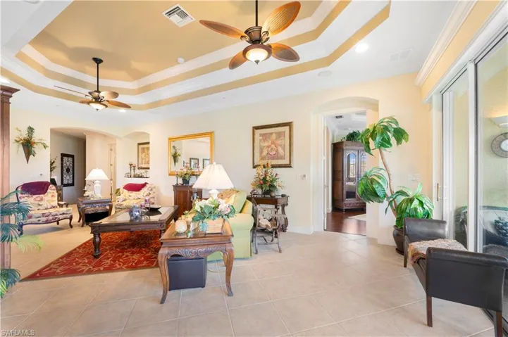 Living room featuring a raised ceiling, crown molding, arched walkways, and ceiling fan