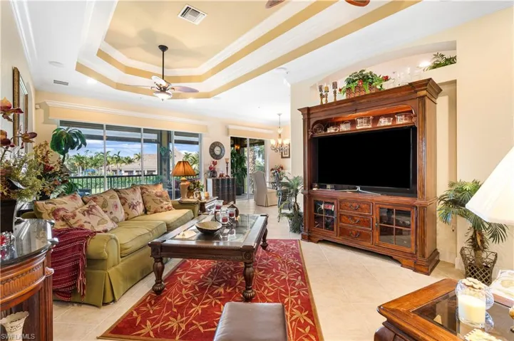 Living room featuring a tray ceiling, crown molding, a ceiling fan, light tile patterned flooring, and a chandelier