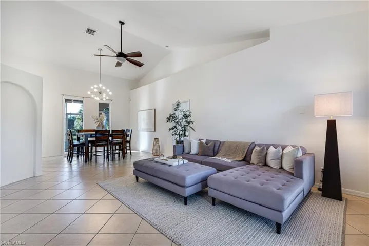 Living area featuring light tile patterned floors, high vaulted ceiling, ceiling fan, and a chandelier