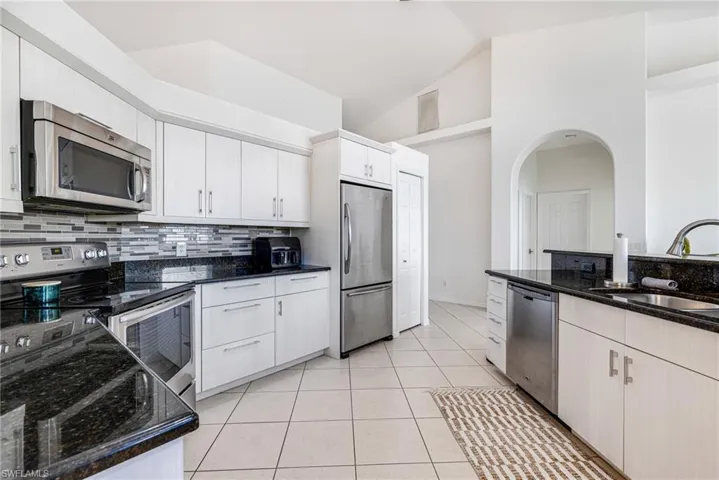 Kitchen with appliances with stainless steel finishes, dark stone counters, tasteful backsplash, white cabinetry, and light tile patterned floors