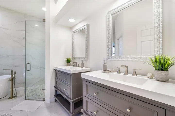 Bathroom with two vanities, a marble finish shower, a soaking tub, and light marble finish floors