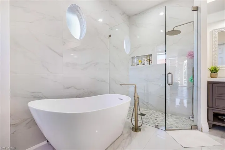 Bathroom with a marble finish shower, vanity, and a freestanding tub