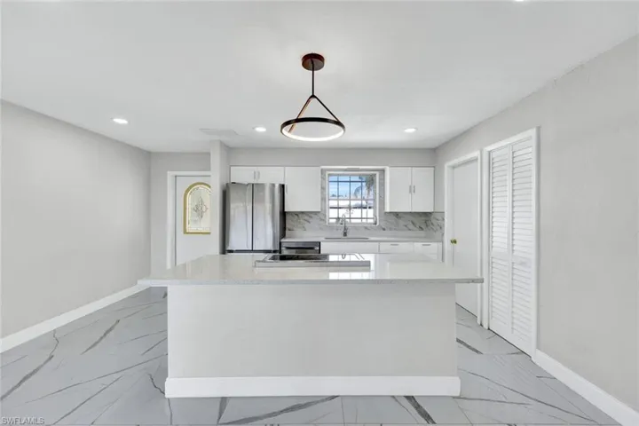 Kitchen featuring baseboards, white cabinets, a sink, and freestanding refrigerator
