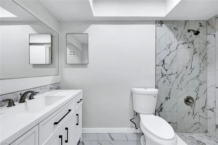 Bathroom with a marble finish shower, toilet, marble finish floor, and vanity