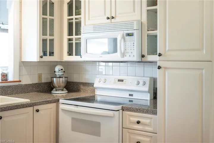 Kitchen featuring white appliances, dark countertops, glass insert cabinets, decorative backsplash, and white cabinets