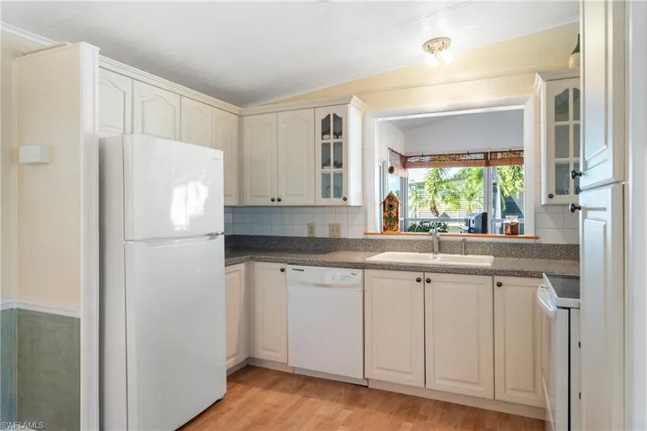 Kitchen with white appliances, glass insert cabinets, light wood-style flooring, vaulted ceiling, and tasteful backsplash