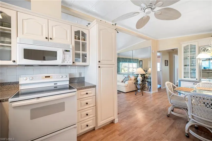 Kitchen featuring white appliances, ornamental molding, glass insert cabinets, light wood finished floors, and cream cabinetry