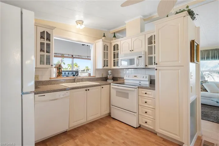 Kitchen featuring glass insert cabinets, white appliances, light wood finished floors, decorative backsplash, and crown molding