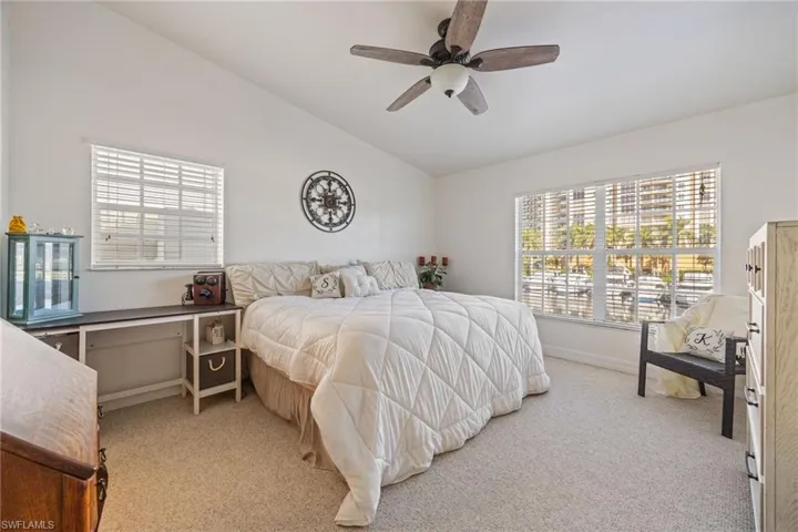 Carpeted bedroom featuring vaulted ceilings, a ceiling fan with light fixture, and two large windows with horizontal blinds