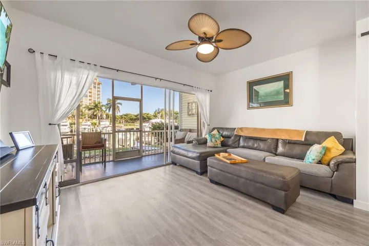 Spacious living area featuring light wood-finish flooring, a ceiling fan with integrated lighting, and a screened balcony
