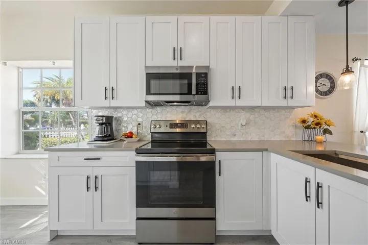Modern kitchen featuring white shaker-style cabinetry, stainless steel appliances, a geometric tile backsplash, and light-toned countertops