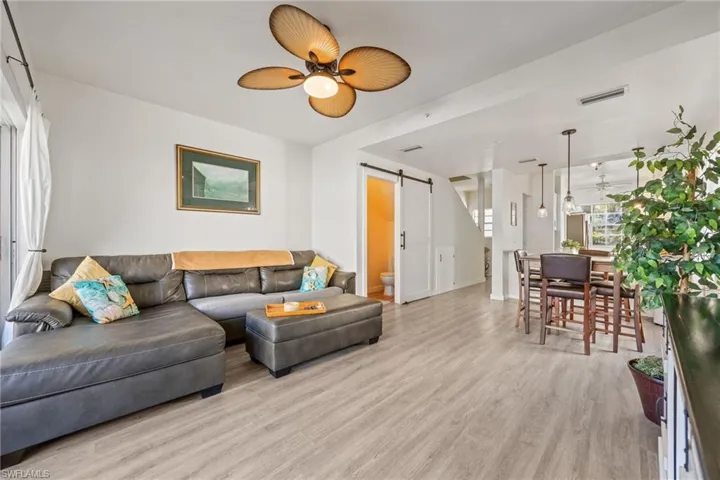 Open-concept living area featuring light wood-finish flooring, a decorative ceiling fan, and a barn door entry
