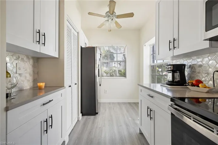 Galley kitchen featuring white shaker cabinetry with black hardware, hexagon tile backsplash, light grey countertops, and wood-finish flooring