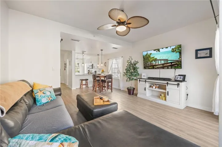 Open-concept living area with wood-finish flooring, a ceiling fan with integrated lighting, and white walls
