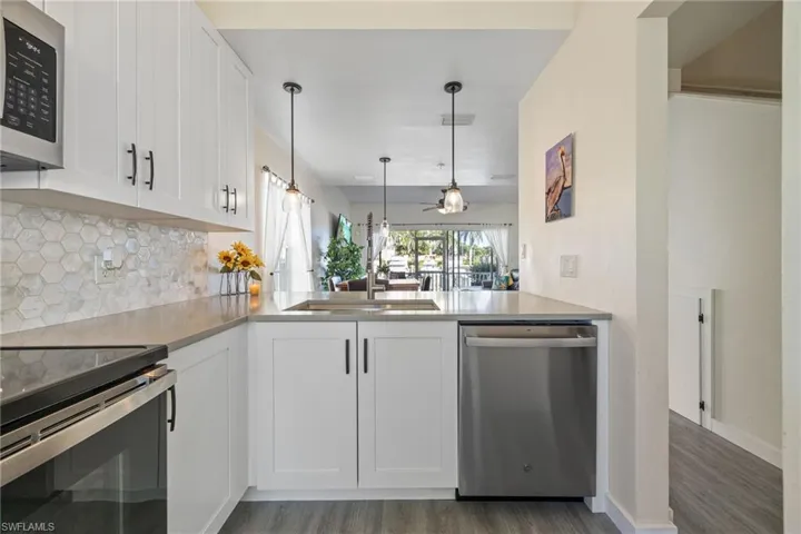 Kitchen featuring white shaker-style cabinetry, stainless steel appliances, a hexagonal tile backsplash, and light-toned countertops