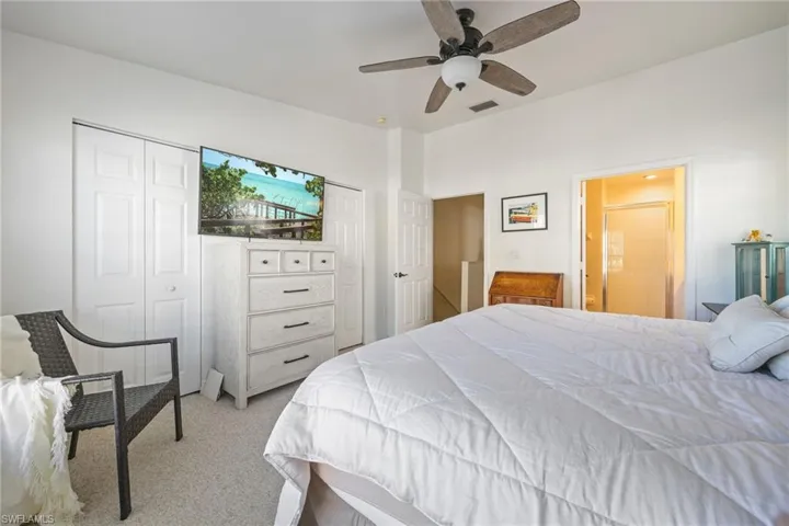 Carpeted bedroom featuring a ceiling fan with integrated lighting, bi-fold closet doors, and an entryway to an adjacent bathroom with a glass-enclosed shower