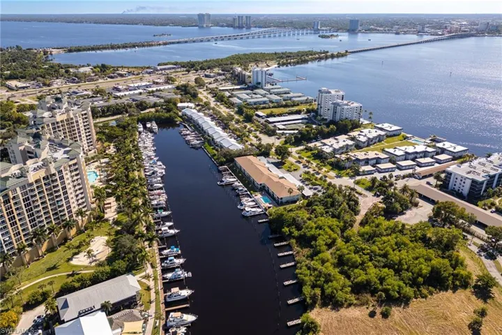 Aerial perspective showcasing waterfront properties, a marina with numerous docked boats, a prominent bridge spanning a large body of water, and surrounding urban development