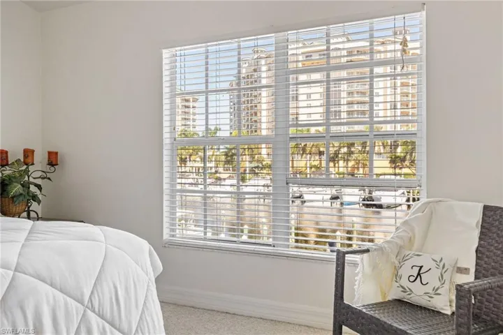 Large window with white blinds and grid panes, offering a water feature and cityscape backdrop