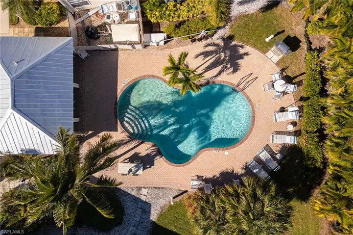 Freeform swimming pool surrounded by a brick paver deck, lush landscaping, and mature palm trees