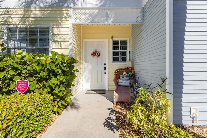 Entryway featuring a white door, yellow horizontal siding, a white lattice overhang, a window with white trim, and a concrete pathway
