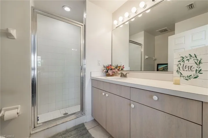 Bathroom featuring a shower with glass enclosure, single vanity with light wood-finish cabinetry, and a large wall-mounted mirror with integrated vanity lighting